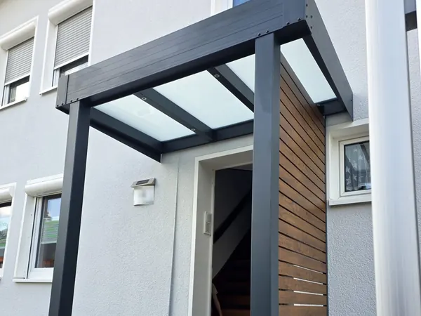 Vordach aus Alu mit Glas über einer Haustür, an der Seite ein Holzpaneel